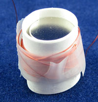 Tape secures copper wire that has been wrapped around a paper tube which holds a stack of circular magnets