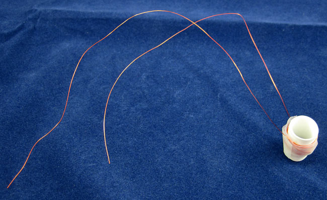 Tape secures copper wire that has been wrapped around a paper tube which holds a stack of circular magnets