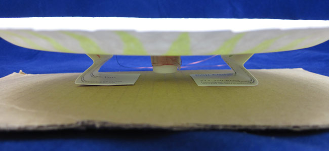 Two bent business cards support a paper plate over a cardboard square
