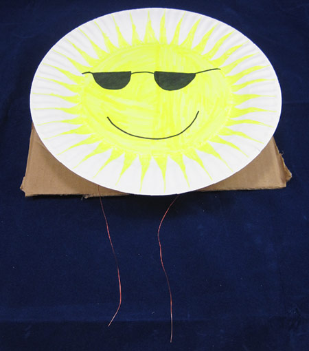 A green-yellow smiley face with sunglasses is drawn onto the surface of a paper plate