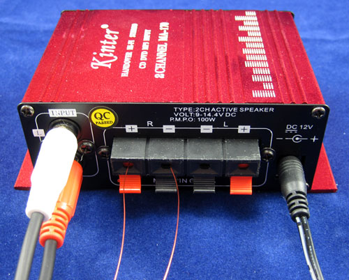 Two RCA plugs, two copper wire leads and a power cable plug into the back of an amplifier