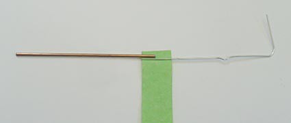 A paperclip bent into an L shape has its longest side taped to a nail sized iron core