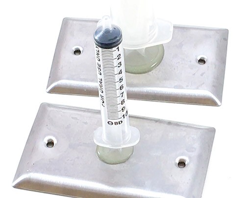 The flat part at the top of a small syringe glued to wall plate. In the background, you see the top of a larger syringe is glued to a second wall plate. 