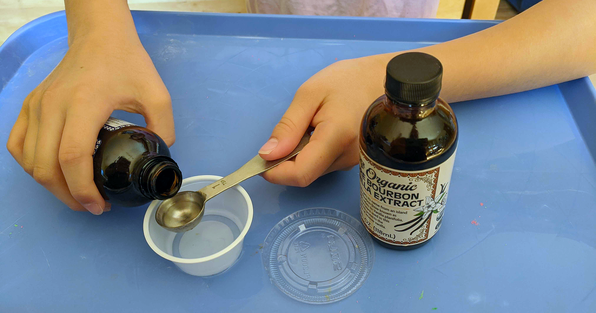 Student measuring vanilla flavoring into a small plastic cup for smell memory experiment