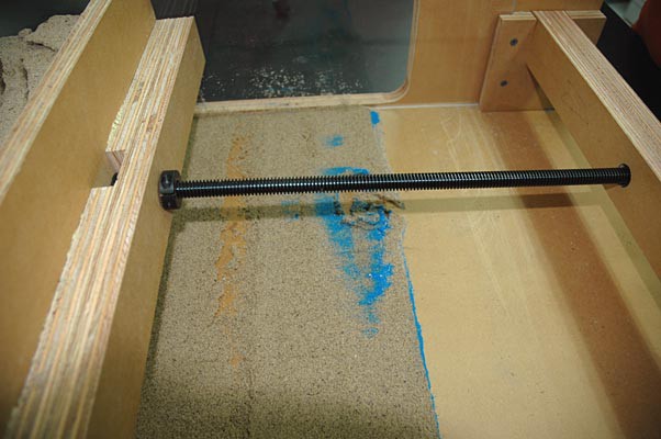 As a wood panel moves to compress sand a trail of sand slips beneath the panel and is left behind