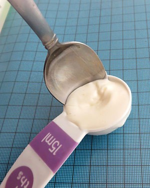 A metal spoon is inserted between the edges of a tablespoon and a white solid inside the tablespoon