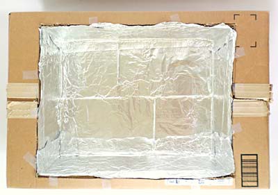 Aluminum foil lines the inside of a cardboard box that is sitting in a larger cardboard box