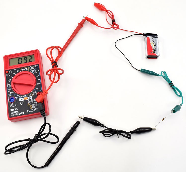 Alligator clips connect the leads of a multimeter to a nine volt battery and a resistor in a closed circuit