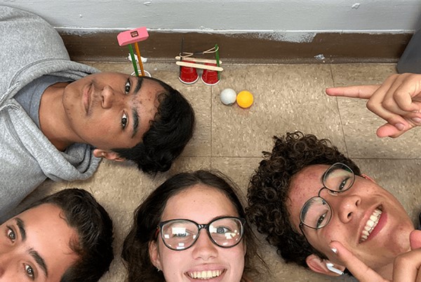 Group of students pointing at their 2020 Engineering submission and smiling