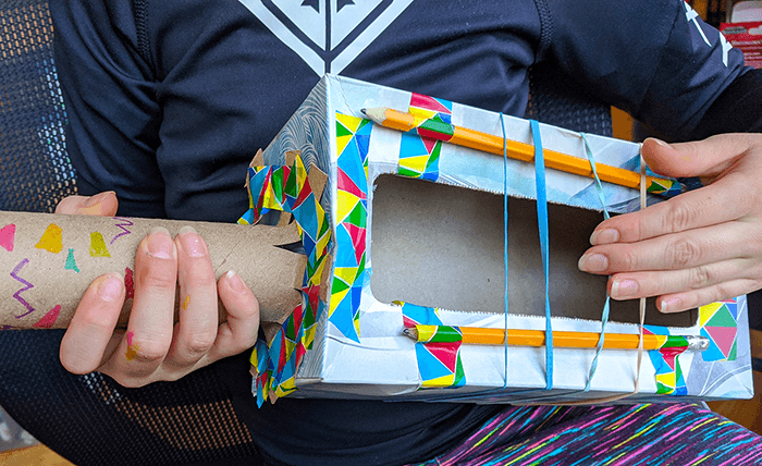 Student holding final rubber band guitar from tissue box and rubber bands and pencils - and decorated