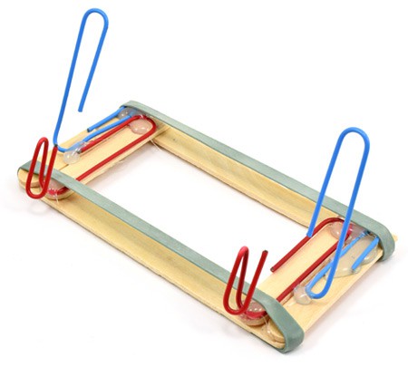 A phone stand is built from popsicle sticks, rubber bands and paper clips