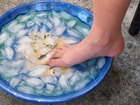 This photo shows a bare foot with the heel resting on the rim of a large bowl of ice water and the toes submerged in the ice water.