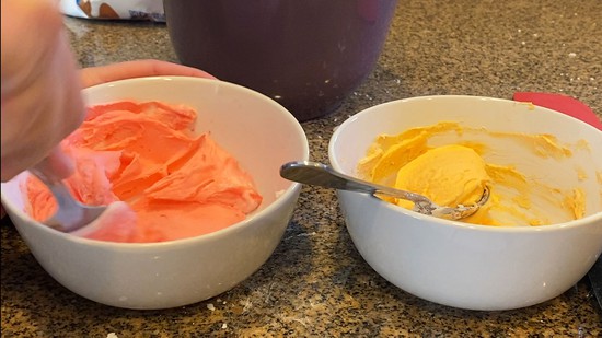  Two bowls of icing, one with red and the other with yellow icing.  