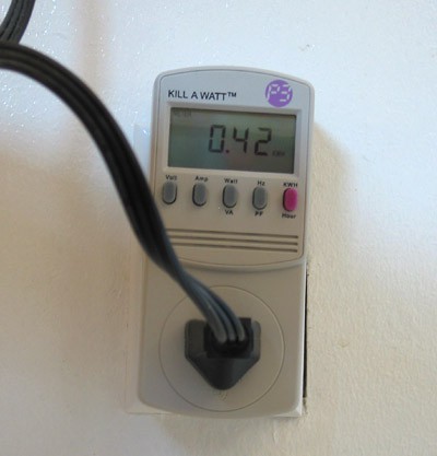 An electric plug is inserted into a Kill a Watt meter which is plugged into a wall outlet