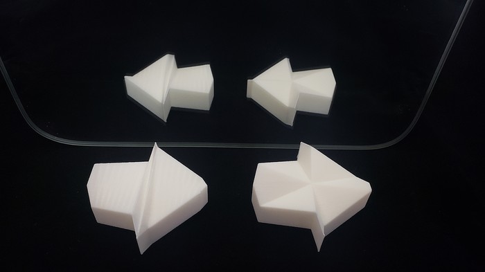 Two versions of the 3D printed impossible arrow that use different triangulation methods for their top surface. One connects triangles across the shape to opposite edges, and one connects triangles to a central point. Both arrows appear to point to the right while their reflection ns in a mirror appear to point to the left.