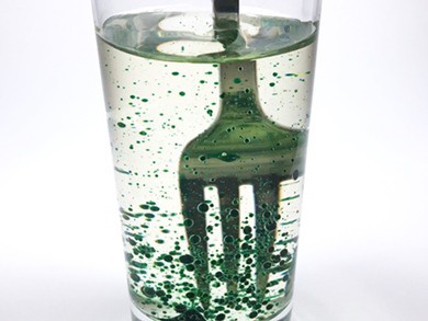 The contents of a glass filled with oil-food-coloring mixture are mixed with a fork.