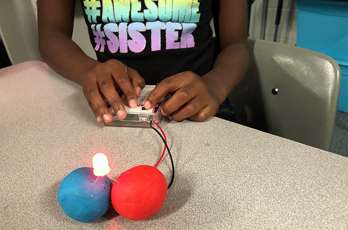 A child assembles a circuit made from an LED, battery pack and two balls of conductive play dough