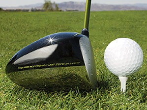 The head of a driver rests at an even height with a golf ball on a tee