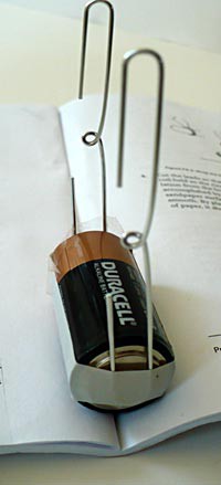 Two paperclips are taped paralle to each other on the top and bottom of a C cell battery