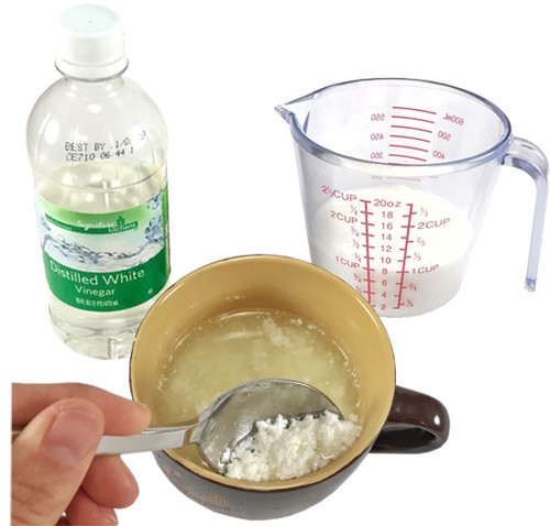 A bottle of vinegar, a cup of milk and a mug filled with milk that is separating into curds and whey