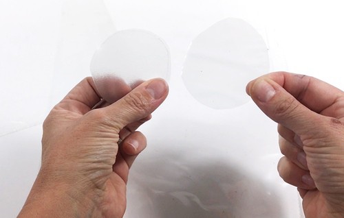 Hands holding two circles cut out from frosted and clear plastic.