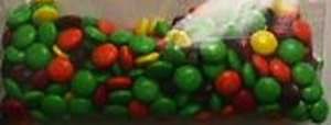 Clear bag full of green M&Ms with a handful of red, orange, and yellow M&Ms interspersed. 