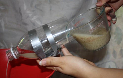Brown liquid is poured through the bottom of a plastic bottle so that it flows over a magnet taped to the outside