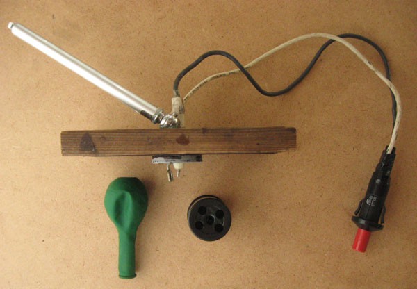 A push-button igniter, film canister, wooden board, deflated balloon and pressure gauge are assembled