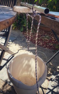 A picture of a panel, its sides barely resting on the edges of two tables. A dowel rests on the panel, parallel with the gap between the tables.  A bucket hangs under the panel, it is attached to the dowel with rope.  