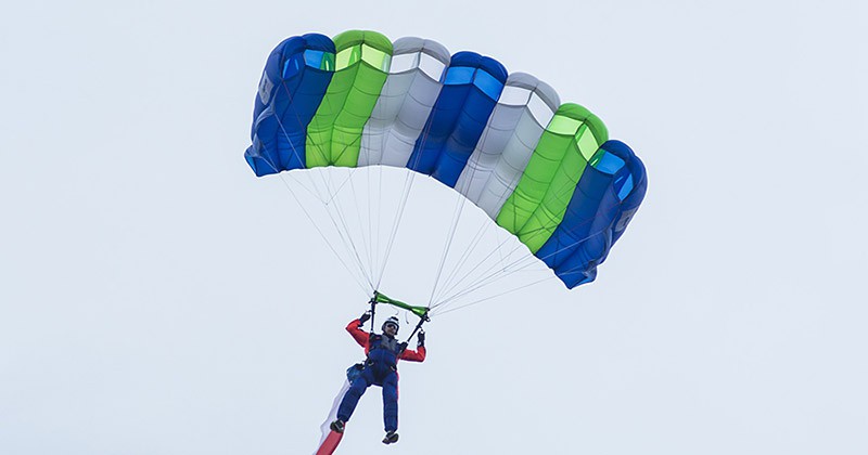  Parachuter with open green, white, and blue parachute high up in the sky. 