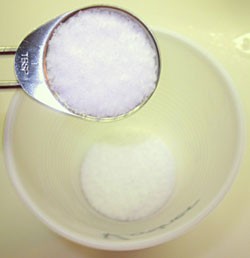 A tablespoon of salt is poured into a plastic cup