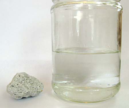 A limestone rock next to a glass jar filled with a clear solution