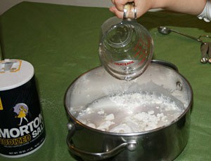 Liquid from a measuring cup is added to white powder in a pot