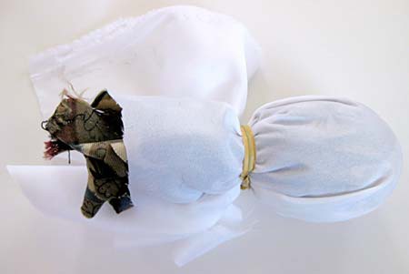 White cloth covers an egg that is wrapped in a tie and is secured with a rubber band