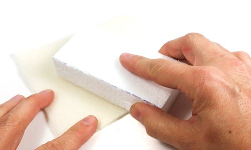 Hands holding a piece of Styrofoam and rubbing it against a piece of wool.