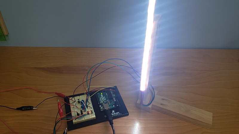 An Arduino Uno next to a breadboard connects to a bright white strip of LEDs that is mounted vertically to a piece of wood 