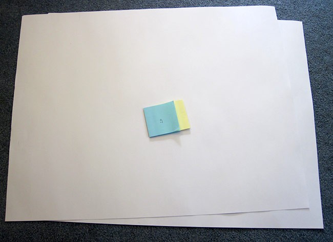 Two pads of blue and yellow paper with the paper interlaced on a piece of poster board