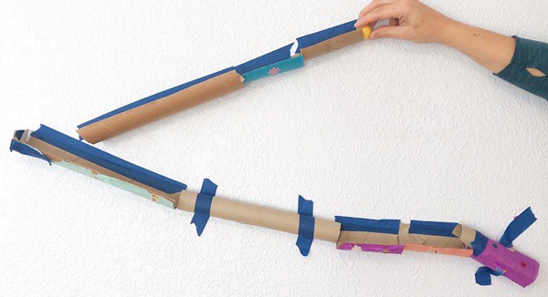 Several cardboard tubes taped to a wall to make a marble run. A person is placing a marble at the top of the track.