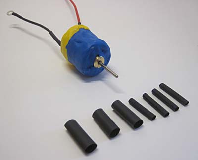 A water-proofed DC motor next to seven pieces of heat shrink tubing