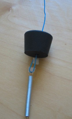 A bent paperclip is inserted through the center of a rubber stopper and has a spring attached to one end
