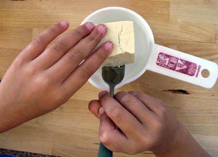 A fork is used to lift a piece of tofu from a measuring cup