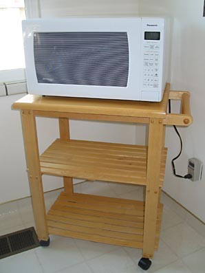 A microwave sits on a wooden cart