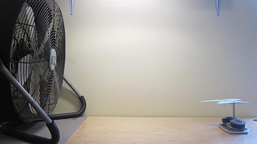 A paper butterfly cutout on a popsicle stick support structure in front of a large fan