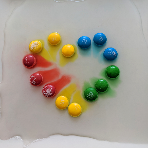 Candies placed in a heart shape and color diffusion happening after water is added