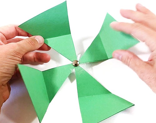Paper pinwheel made from four paper triangles with a thumbtack through its center. 