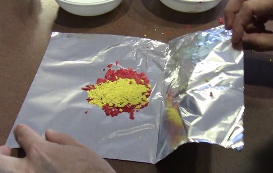 Crayon shavings on aluminum foil compressed into flat layers, forming a sedimentary 