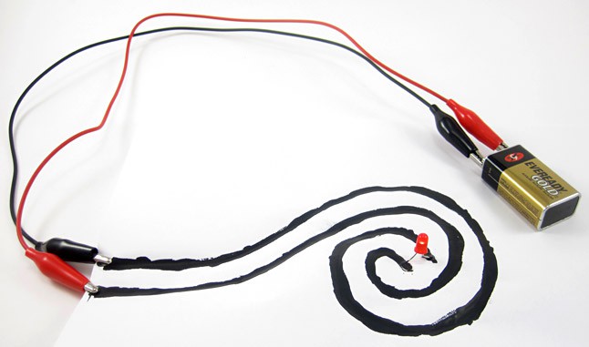 A paper circuit made from a battery, alligator clips, electric paint in a spiral pattern and an LED