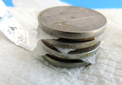 Four layers of a penny, paper towel square, and nickel are stacked on top of each other