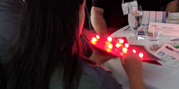 A woman holding a paper sheet covered in red LEDs
