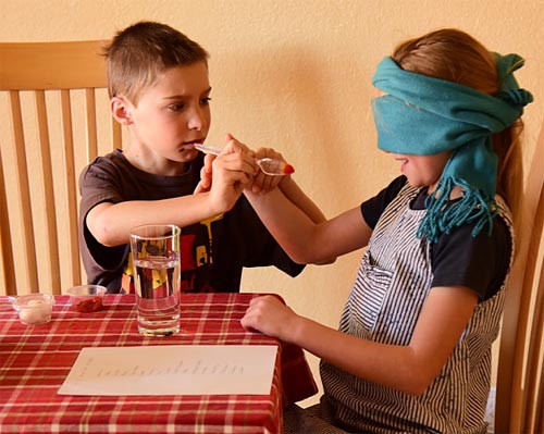 A child passes a spoon holding food to the hand of another child who is blindfolded